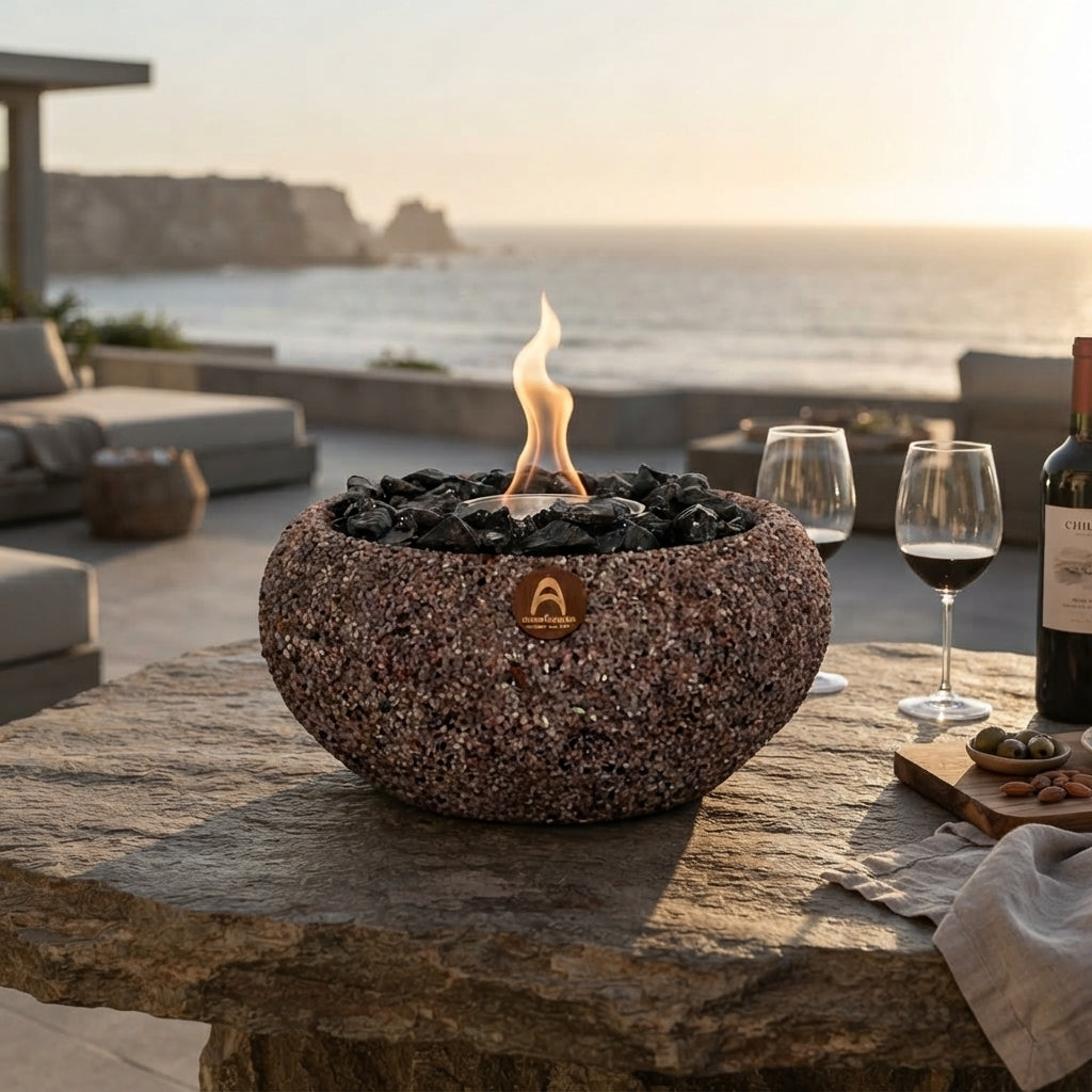Costa Grande Terracota Obsidiana encendido sobre una mesa de piedra con copas de vino, frente al mar